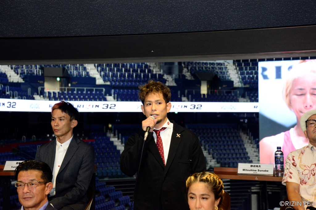 Mitsuhisa Sunabe holds a microphone while speaking at a press conference inside the Okinawa Arena.